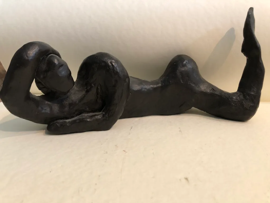 A black clay figure reclining in profile against a white wall.