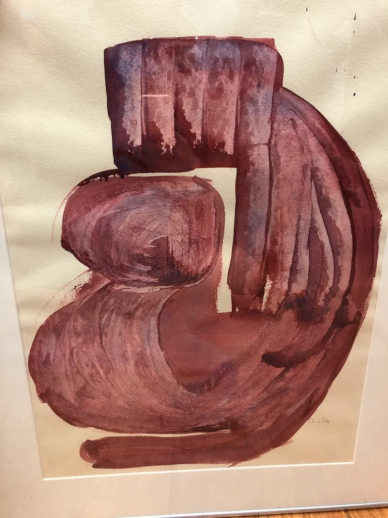 A framed painting: a thick maroon form curling in on itself against cream paper.