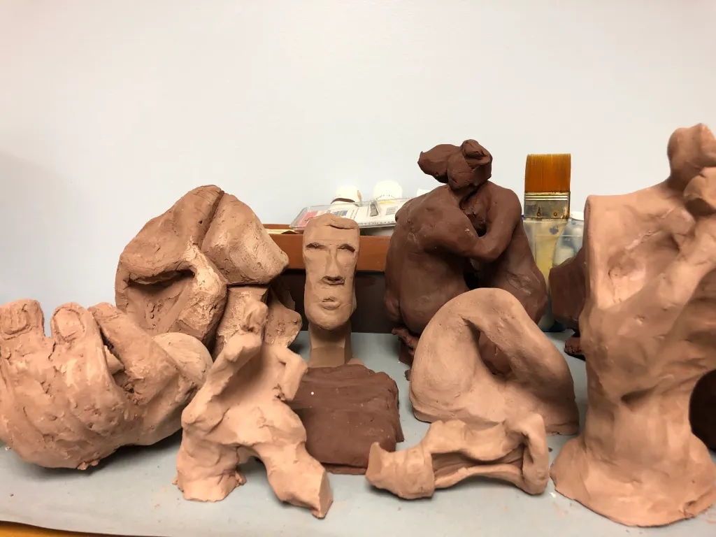 A dark clay torso lying on a white surface, its hollows turned toward the light.