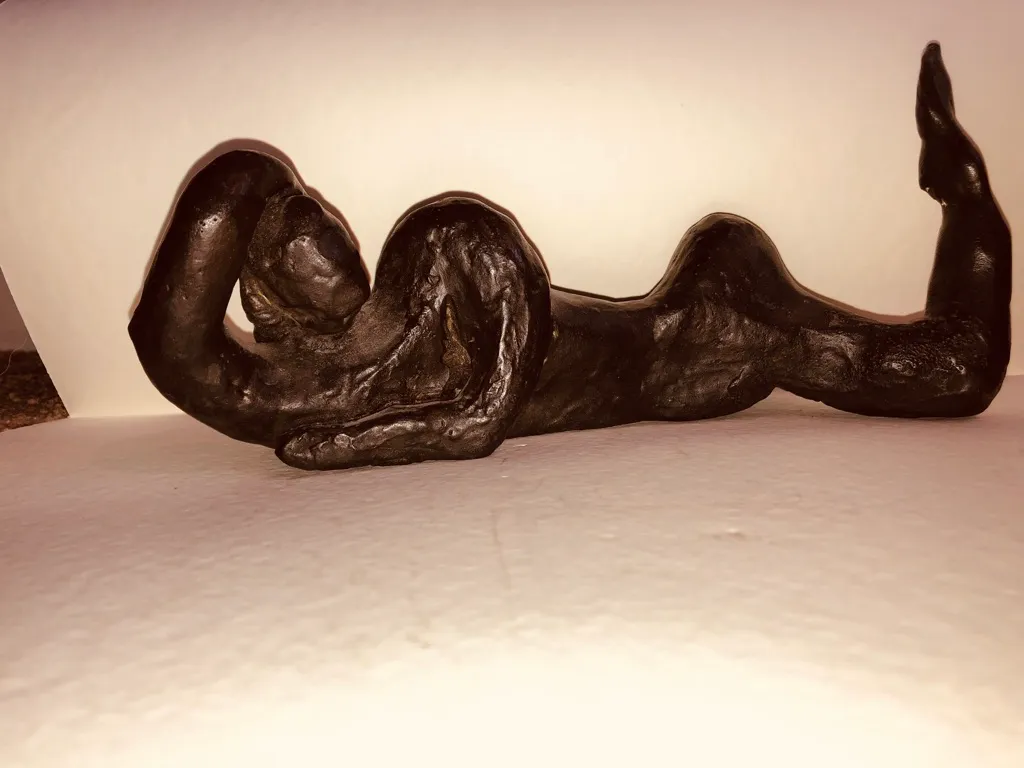 The black reclining figure against a warm wall, seen slightly from below.