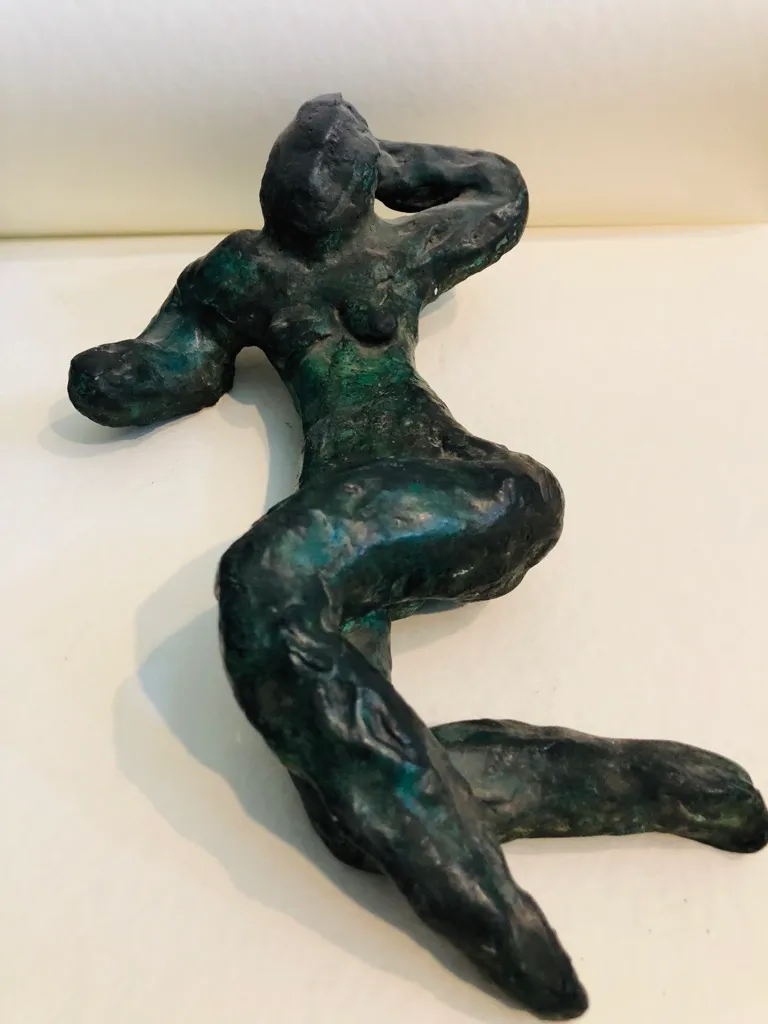 The green-patinated reclining figure seen from the side, the raised knee catching the light.
