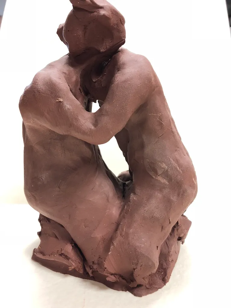 The kneeling clay figure from the front, its head bowed onto its arms.
