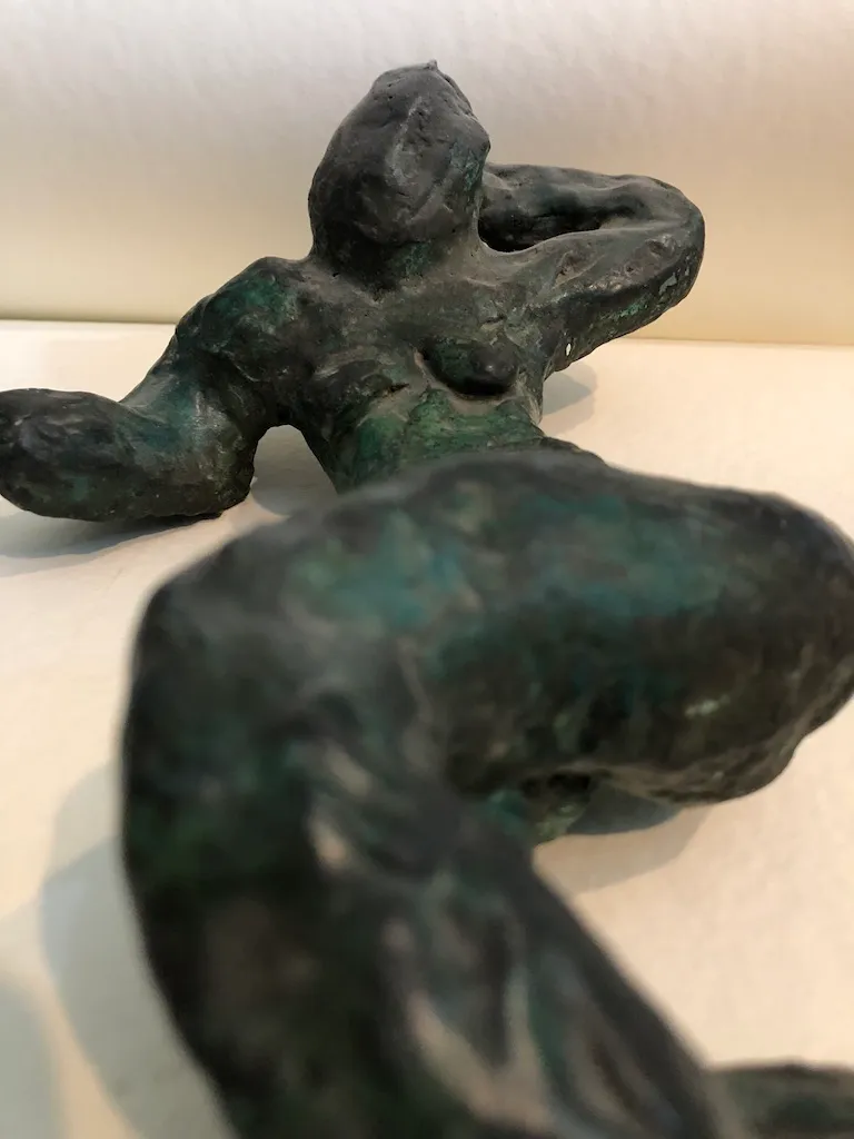 The green-patinated reclining figure photographed low and close, the near leg filling the foreground.